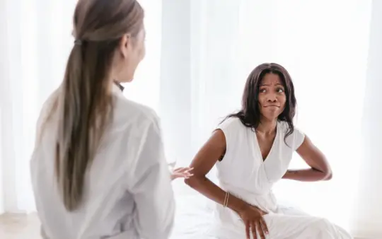 Woman with back pain consults her doctor in a clinical setting wearing a white dress.