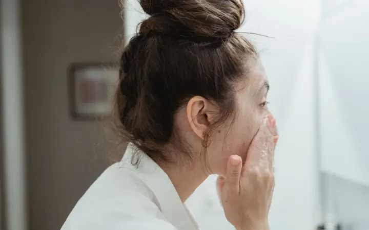 Best face wash for sensitive oily skin: a young woman in a bathrobe follows her skincare routine, washing her face in a
