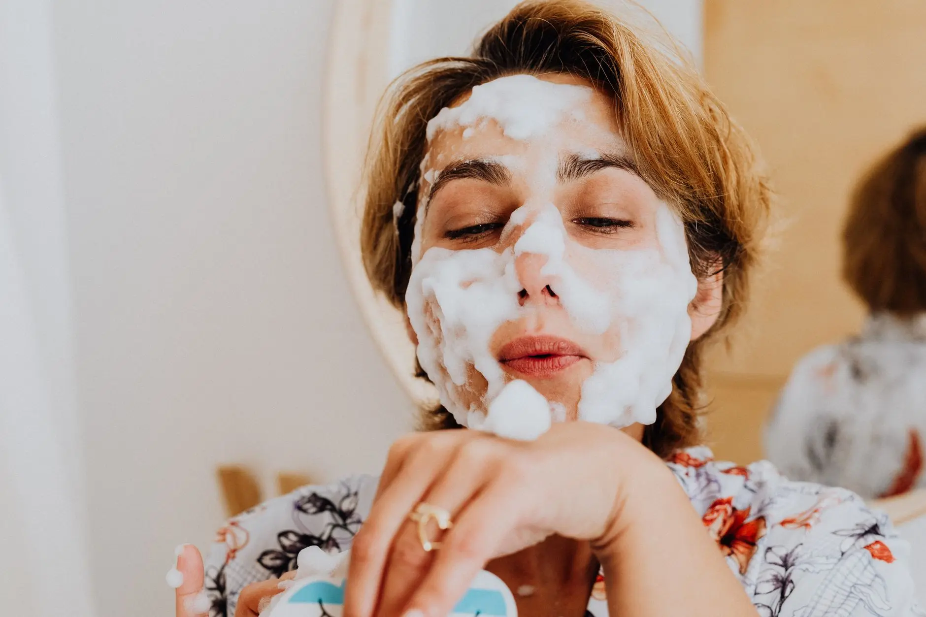 Close-up of a woman applying foamy facial wash, embracing self-care indoors