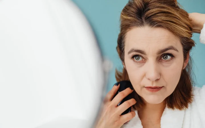 Woman styles her hair while looking into a mirror indoors, focusing on personal grooming.