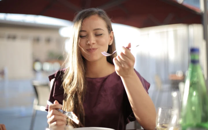 Woman savoring her meal with a smile, dining outdoors in a pleasant setting.