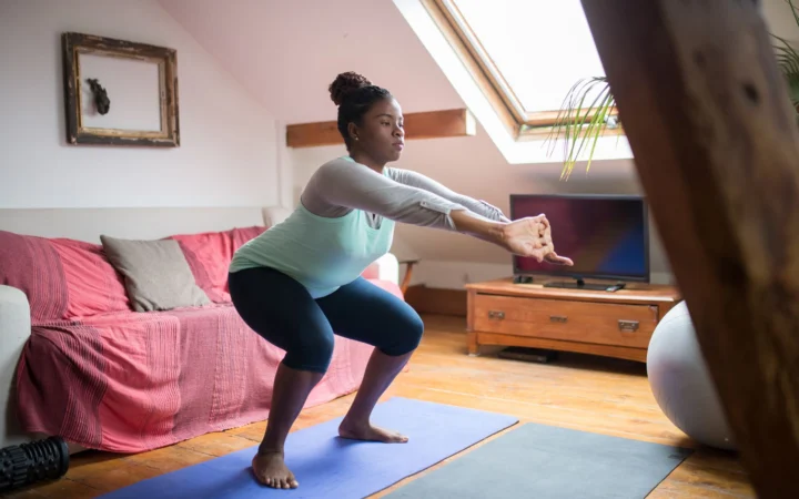 Woman performs squats on a yoga mat in a cozy living room, promoting home fitness and wellness.