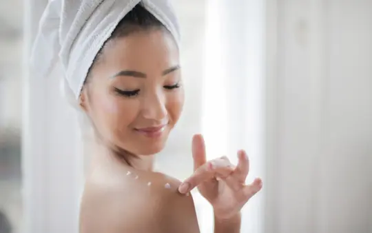 Young woman applying moisturizer indoors, enhancing skin care routine.