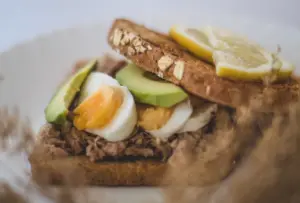 Breakfast recipes high in protein and fiber: close-up of a healthy avocado, tuna, and egg sandwich with lemon slices