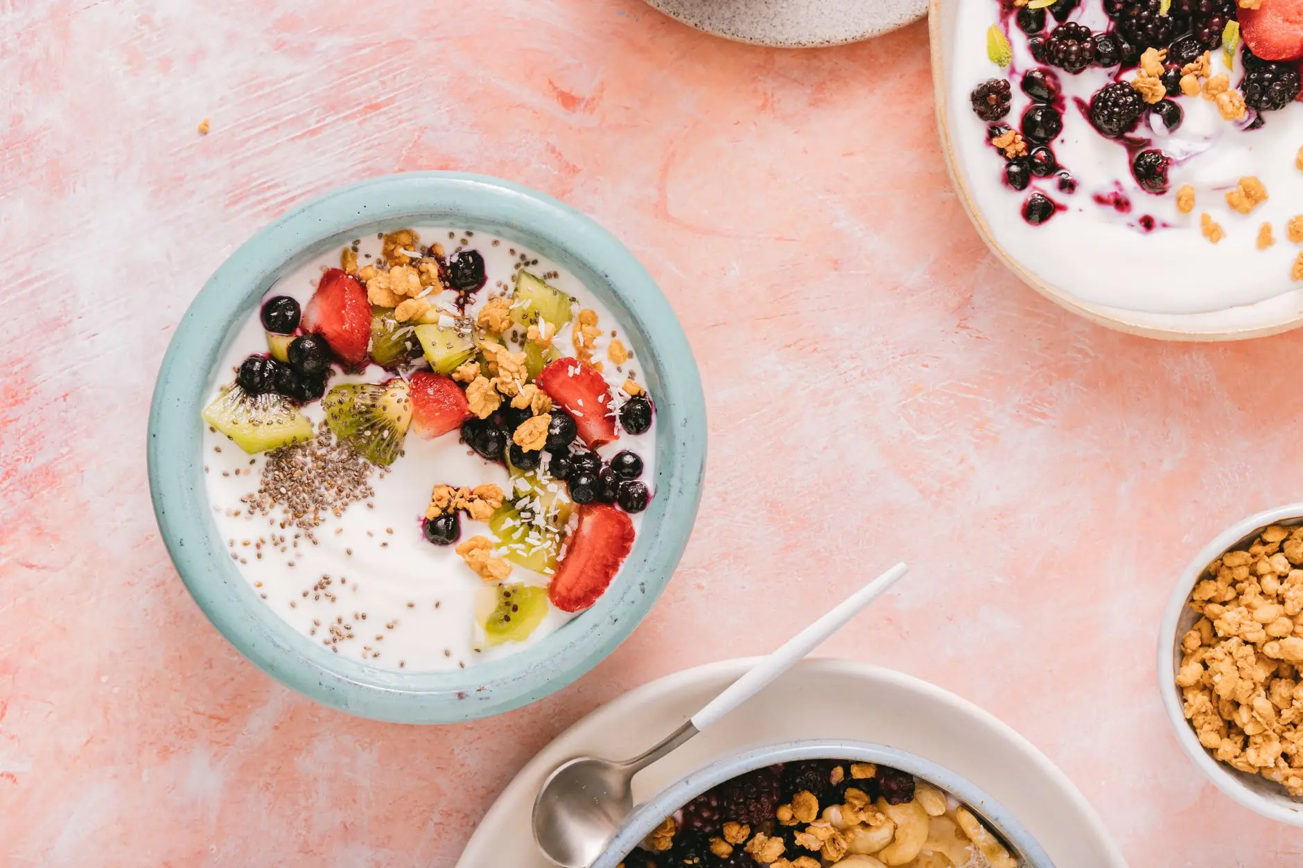 Top view of colorful yogurt bowls topped with fresh berries and granola on a rustic background