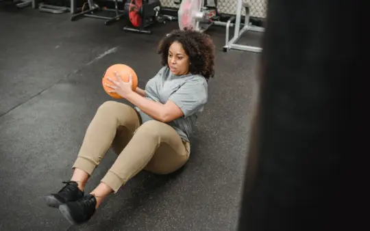 From above of plus size African American female with ball exercising in modern gym