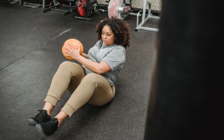 From above of plus size African American female with ball exercising in modern gym