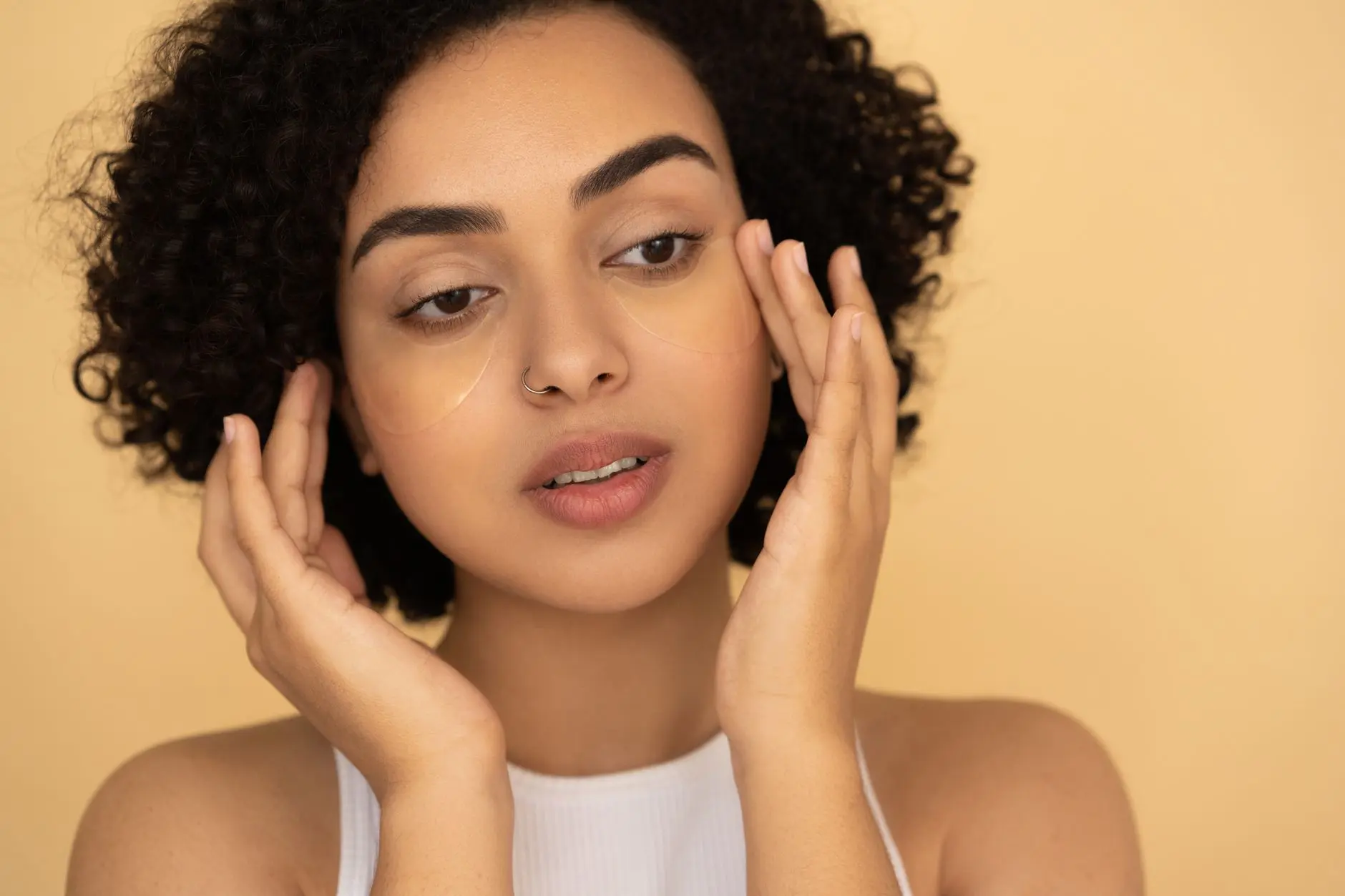 Close-up of a woman applying under-eye mask in a studio setting, focusing on skincare and wellness