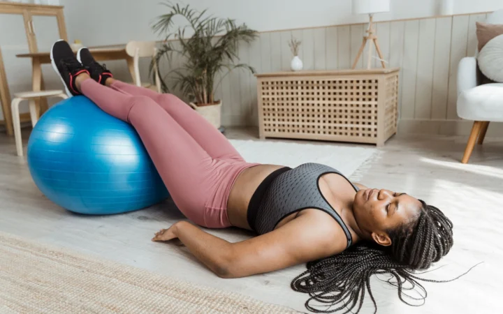 African American woman lying on gym ball in home setting, focusing on fitness and relaxation.