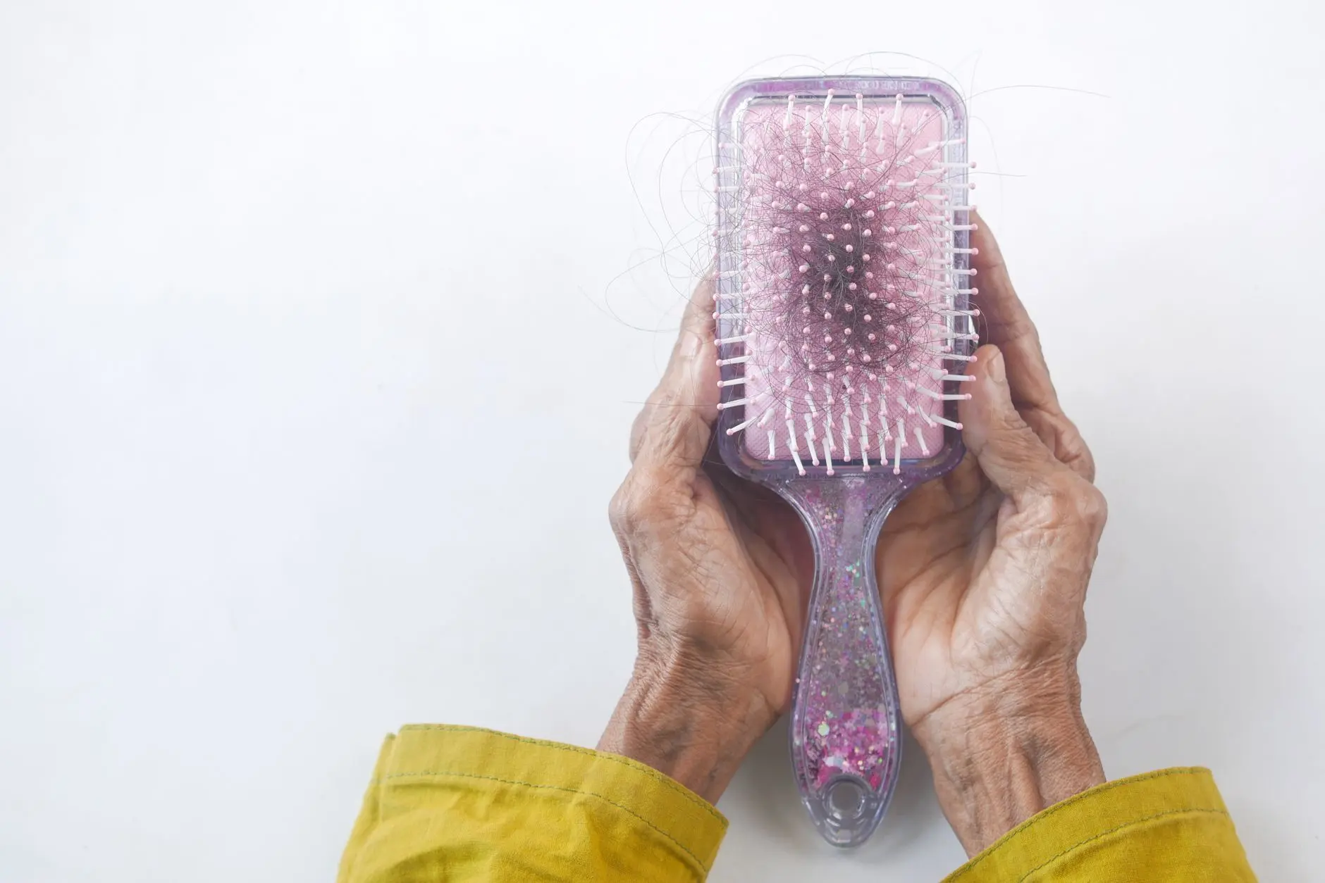 Close-up of senior hands holding a hairbrush with hair strands against a white backdrop
