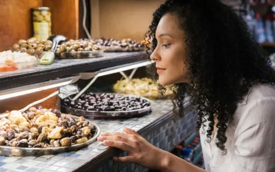 Woman observes a display filled with a variety of olives and other foods.