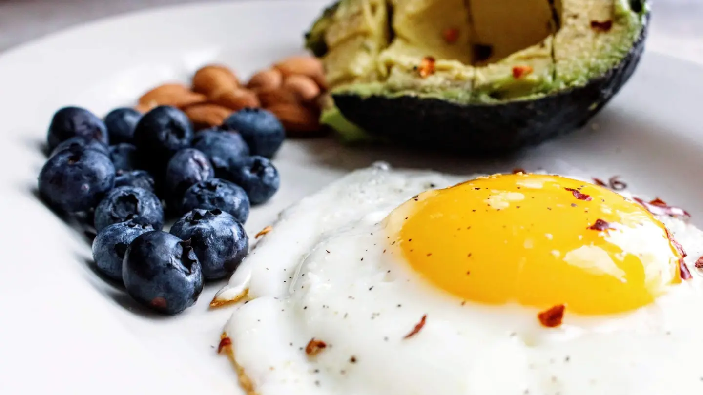 Foods with low carbs and high fiber: a nutritious breakfast featuring a fried egg, avocado, blueberries, and almonds