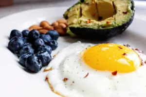 Foods with low carbs and high fiber: a nutritious breakfast featuring a fried egg, avocado, blueberries, and almonds