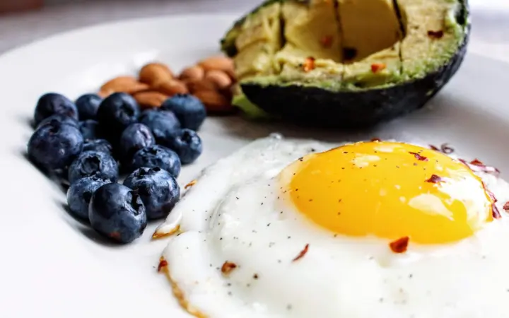 Foods with low carbs and high fiber: a nutritious breakfast featuring a fried egg, avocado, blueberries, and almonds