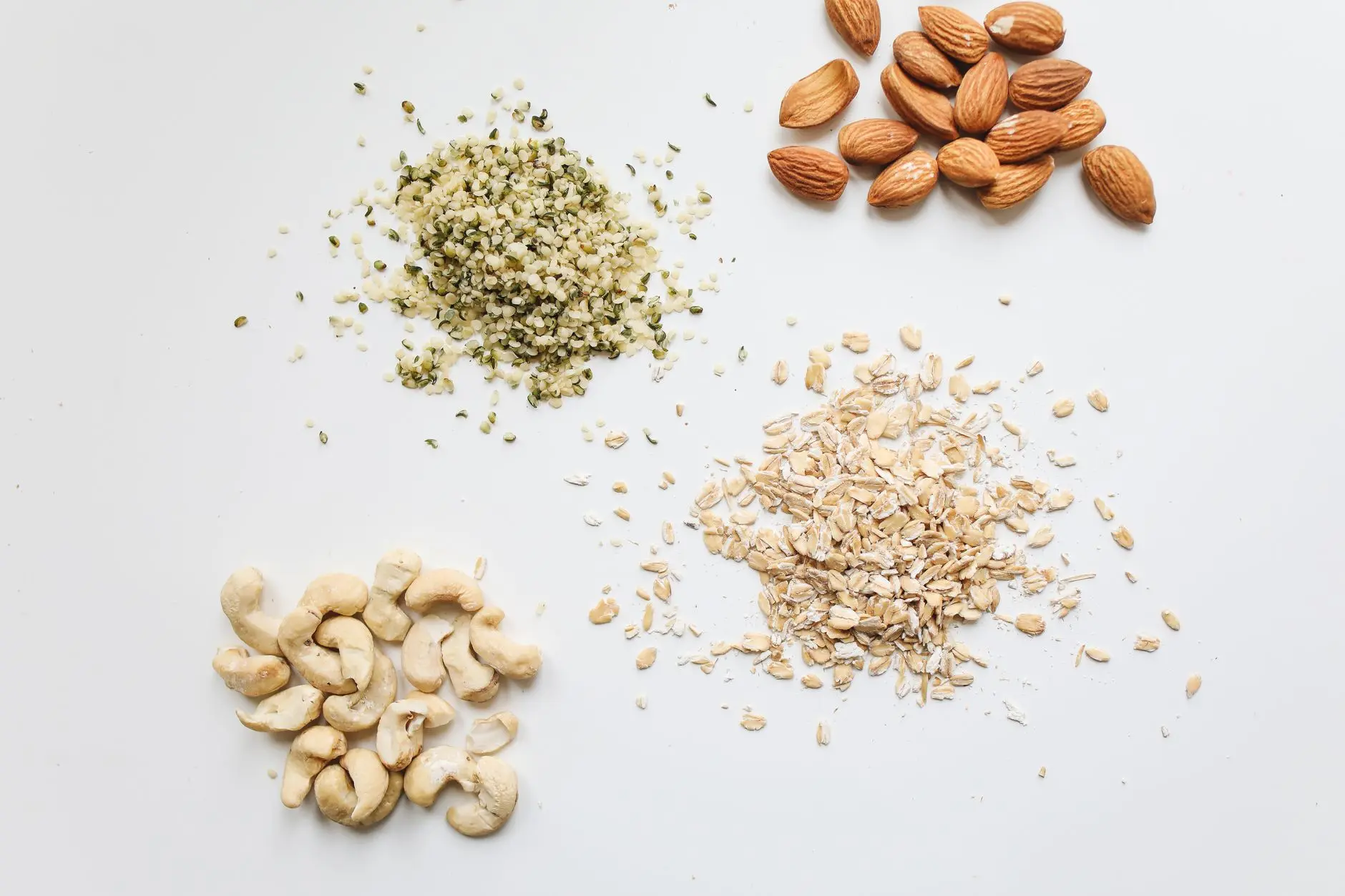 Top view of almonds, cashews, oats, and hemp seeds on white background