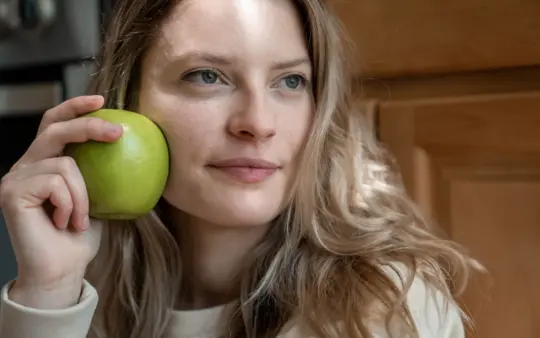 Close-up portrait of a woman indoors holding a green apple, showcasing natural beauty and health.