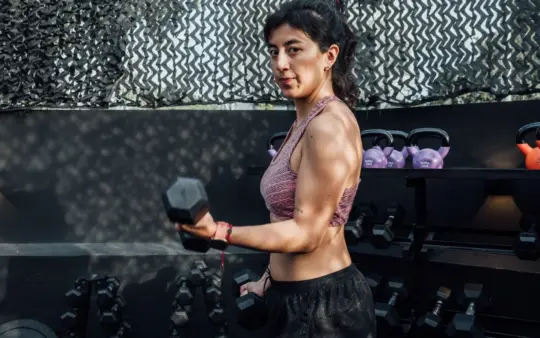 Determined woman lifting dumbbells in an outdoor gym, embracing a healthy lifestyle.
