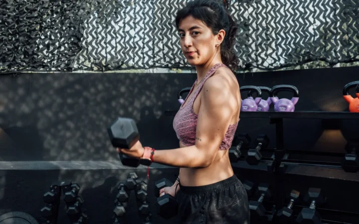 Determined woman lifting dumbbells in an outdoor gym, embracing a healthy lifestyle.