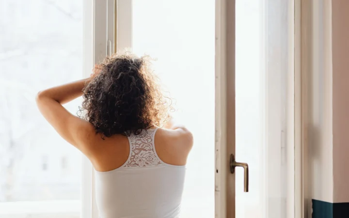 Woman enjoying a peaceful morning, standing by a window, embracing the warm sunlight.
