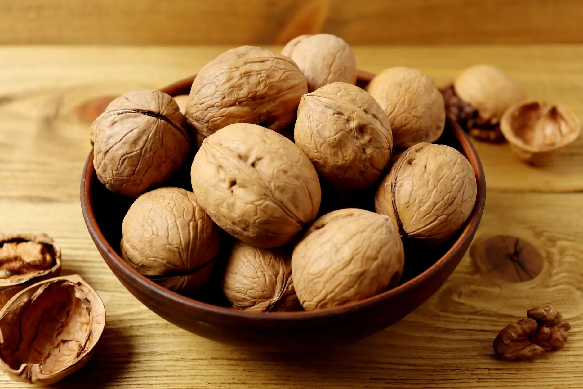 A close-up of whole organic walnuts in a rustic wooden bowl on a wooden table