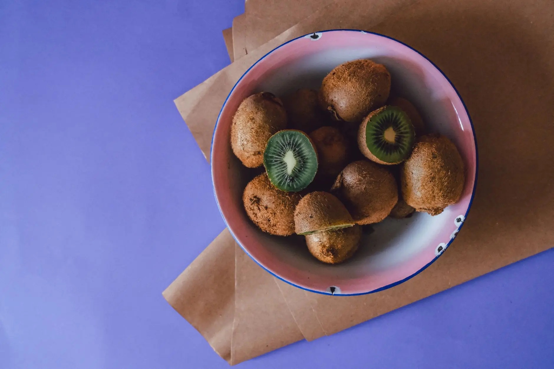 High-angle view of a bowl filled with fresh kiwifruits on a parchment and purple backdrop