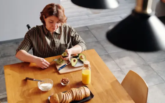 Woman prepares a nutritious breakfast with avocado and orange juice at home.