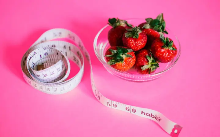 High protein low calorie meals for weight loss: a glass bowl of fresh strawberries paired with a pink measuring tape