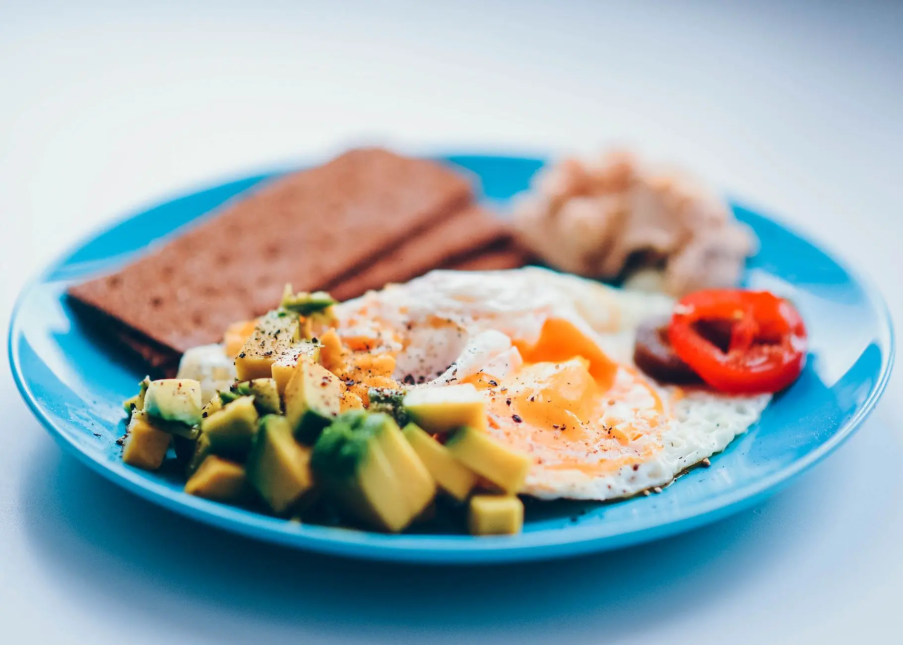 Bright and colorful breakfast featuring fried eggs, avocado, and fresh vegetables on a blue plate