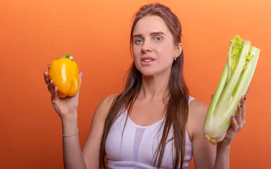 Woman holding yellow bell pepper and celery, showcasing healthy eating.