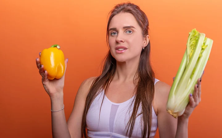 Woman holding yellow bell pepper and celery, showcasing healthy eating.