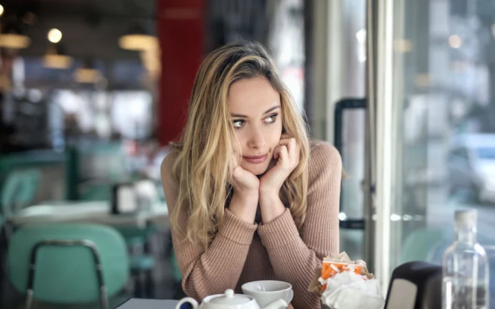 Thoughtful woman with blond hair sitting in a cozy cafГ©, enjoying a hot drink.