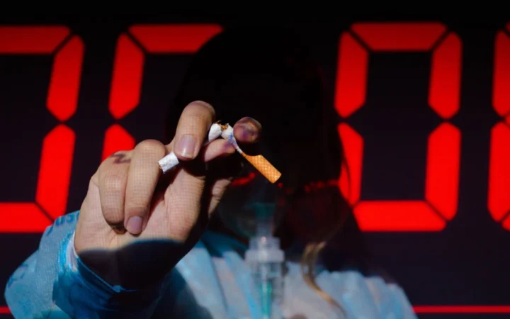 Hand holding a broken cigarette in front of a digital timer, highlighting the urgency of quitting smoking.