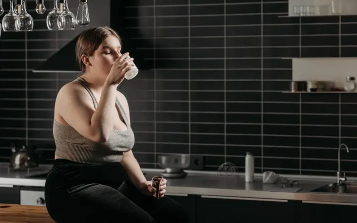 How to lose weight without exercise: woman sitting on kitchen counter drinking milk in a modern setting