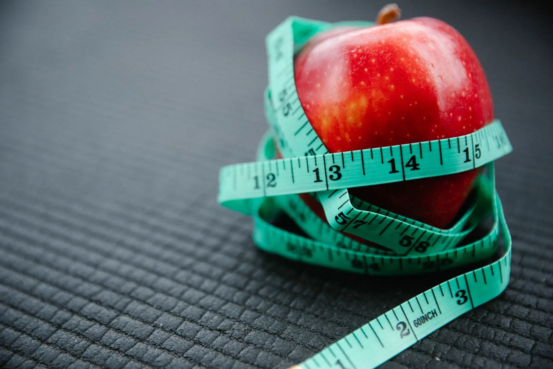 A vibrant red apple encircled by a blue measuring tape, symbolizing health and weight management