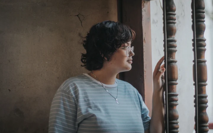 Thoughtful woman with short hair and eyeglasses gazes out a window.