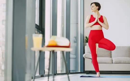 From below of content female in activewear standing on mat in living room while doing yoga exercise and looking away