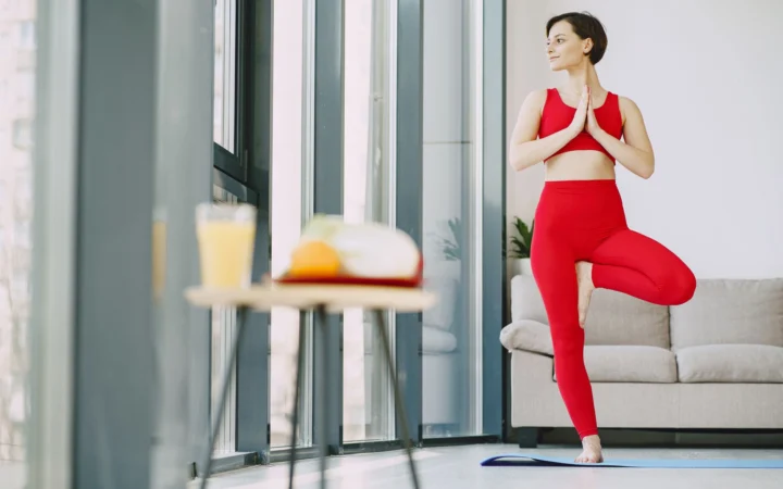 From below of content female in activewear standing on mat in living room while doing yoga exercise and looking away