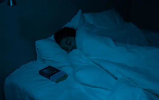 Woman peacefully sleeping with a book under blue night lighting, showcasing a cozy bedtime atmosphere.