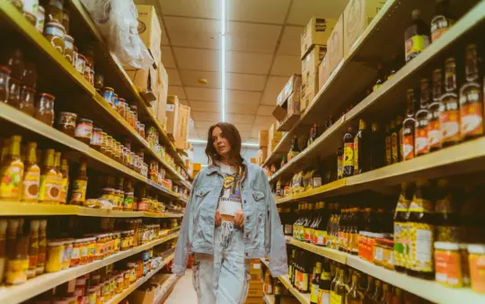 Woman in denim browsing grocery store aisle with products on shelves.