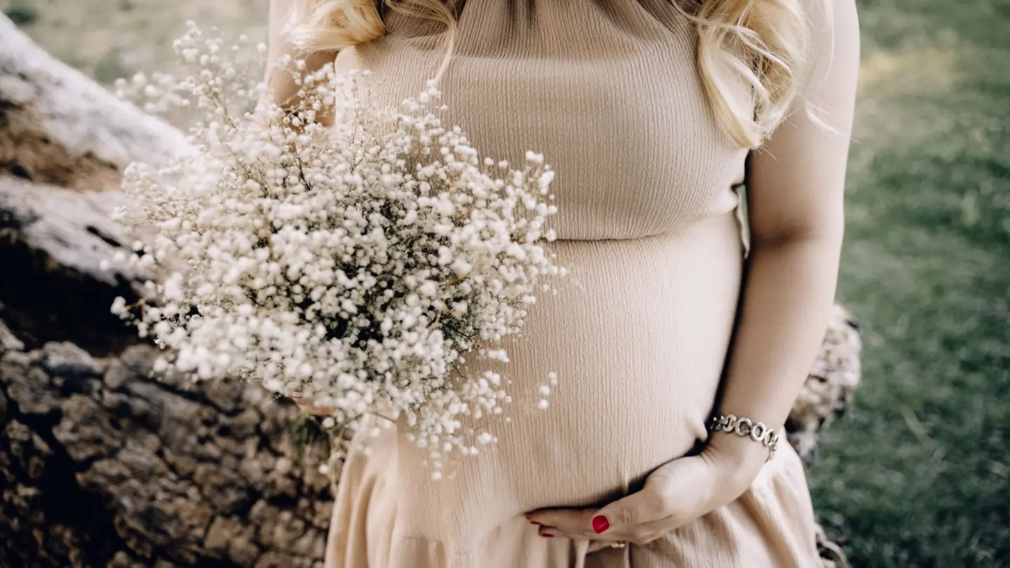 Magnesium supplement for pregnant women: pregnant woman in beige dress holding baby's breath bouquet outdoors