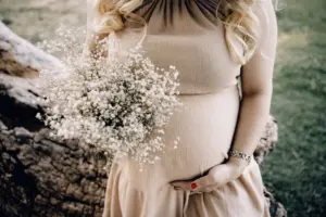 Magnesium supplement for pregnant women: pregnant woman in beige dress holding baby's breath bouquet outdoors