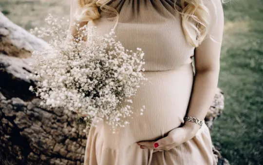 Magnesium supplement for pregnant women: pregnant woman in beige dress holding baby's breath bouquet outdoors