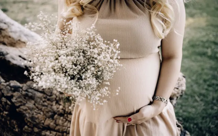 Magnesium supplement for pregnant women: pregnant woman in beige dress holding baby's breath bouquet outdoors