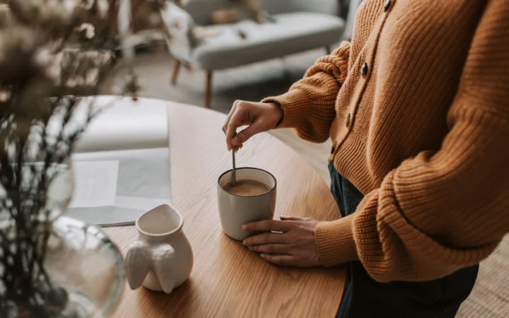 Woman stirs coffee in a cozy home setting, enjoying a warm morning routine.
