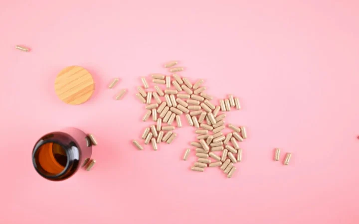 Brown bottle with scattered herbal supplement capsules on a pastel pink background.