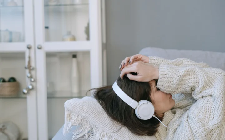 Woman in cozy sweater wearing headphones while lying down indoors, conveying relaxation and comfort.