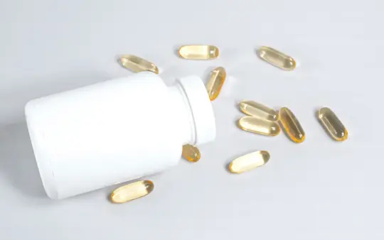 Healthy fish oil capsules spilled from a white bottle on a smooth white surface.