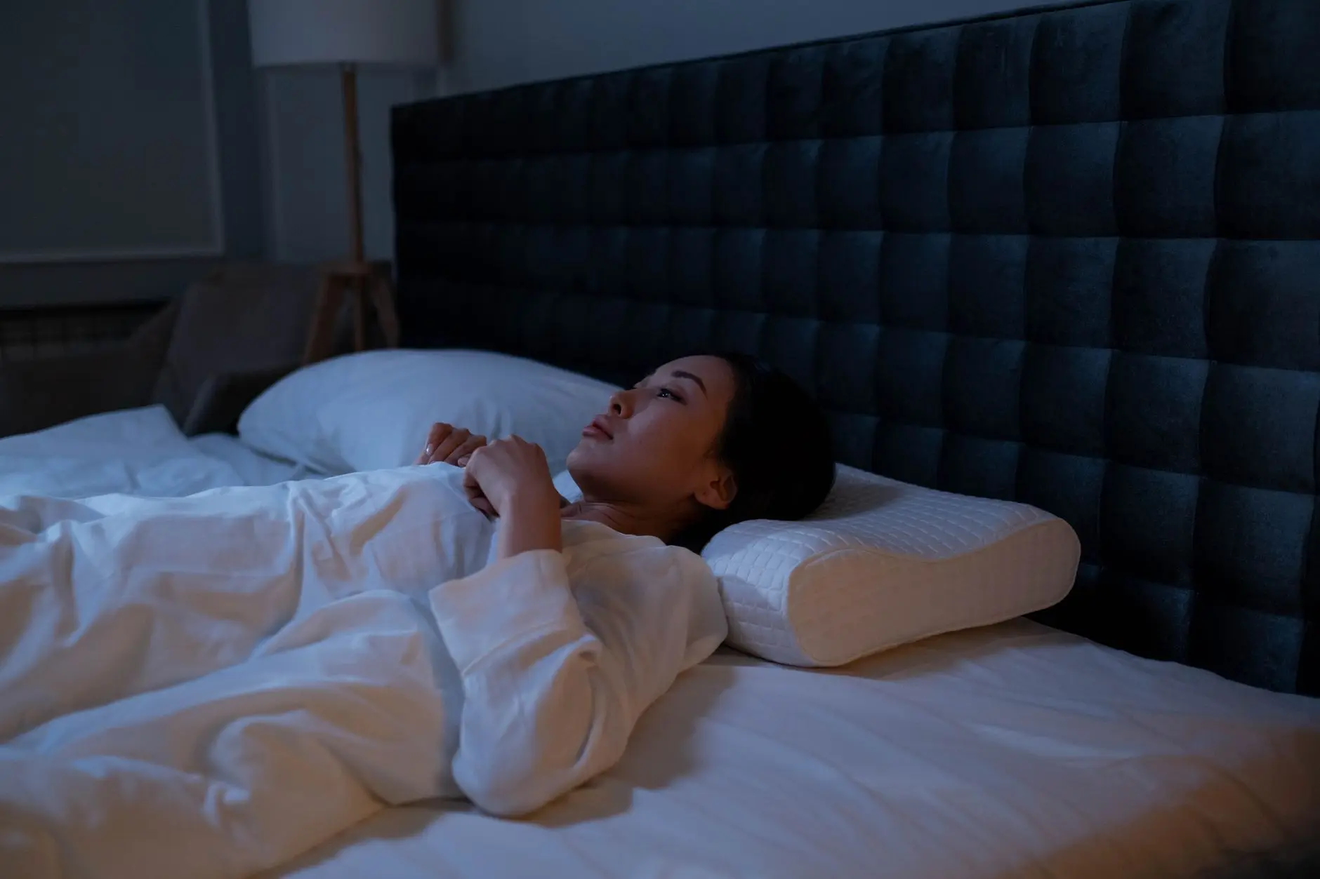 An Asian woman lying awake in bed at night, showing signs of insomnia and sleeplessness
