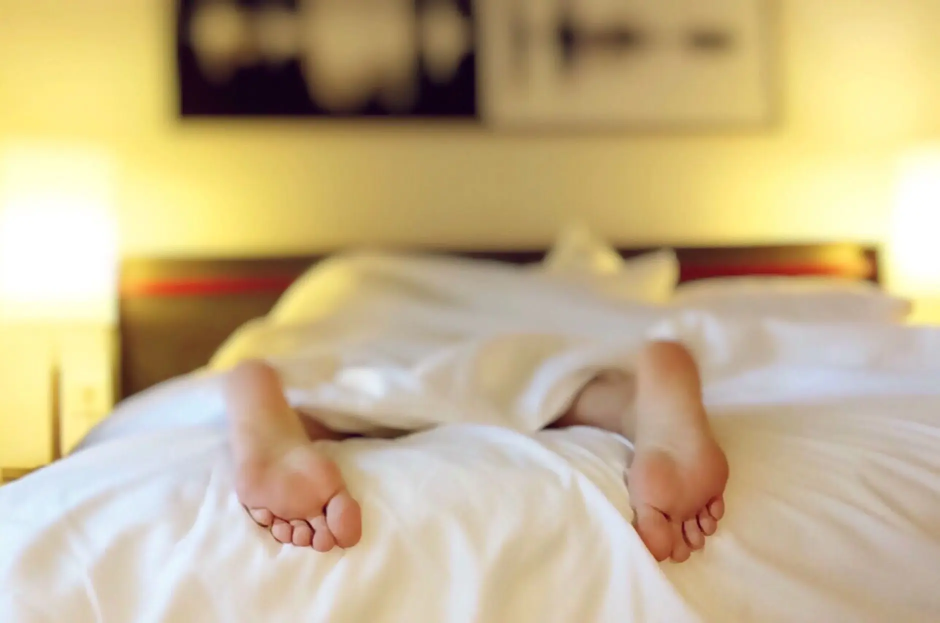 A person relaxing on a bed with feet under white sheets, conveying serenity