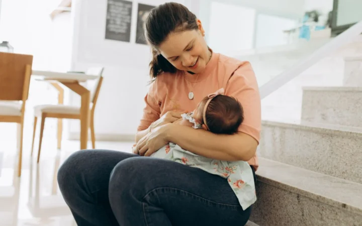 Woman smiling and cradling baby on stairs indoors, portraying warmth and family bonding.